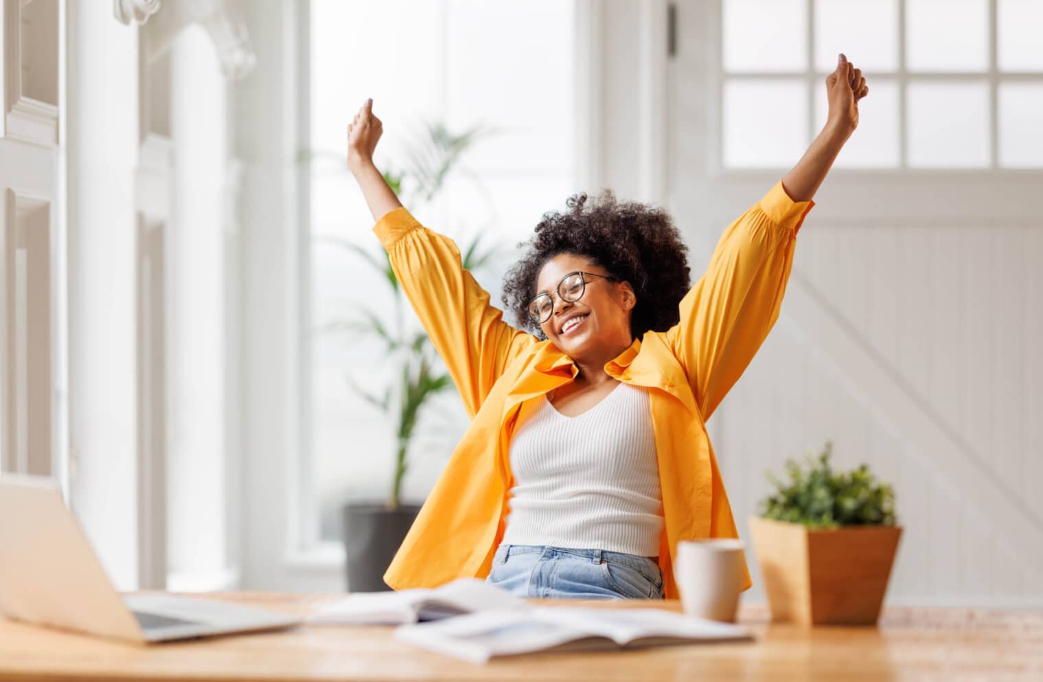 Une femme d'affaires afro-américaine sourit et se réjouit de sa victoire alors qu'elle est assise à son bureau et qu'elle travaille sur l'écran de son ordinateur portable après avoir terminé un projet dans son bureau à domicile.