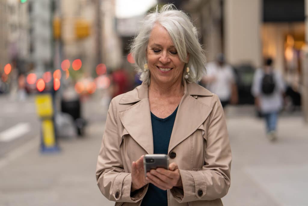 Boomer Frau in der Stadt zu Fuß Straße mit Handy - Generation