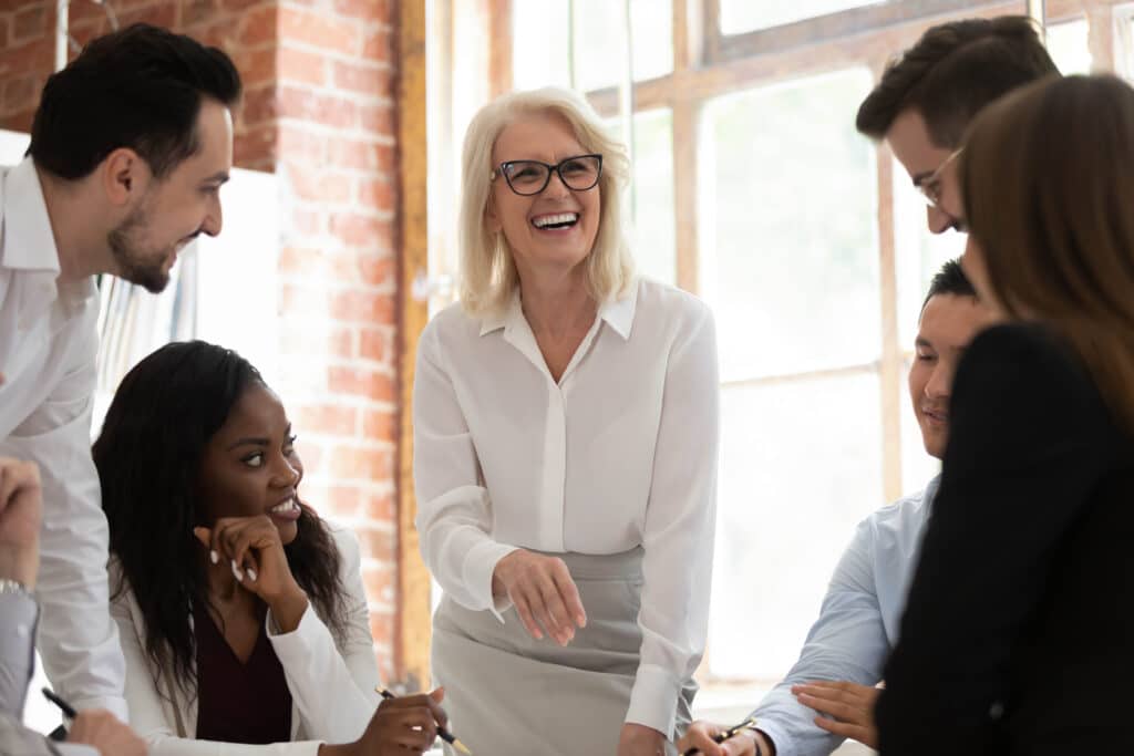 Glückliche multikulturelle Büro junge Mitarbeiter mit alten Mentor Führer Trainer lachend arbeiten zusammen sammeln in Sitzungssaal, diverse Corporate Business-Team mit Spaß in Teamarbeit bei Gruppensitzung engagiert - Generation