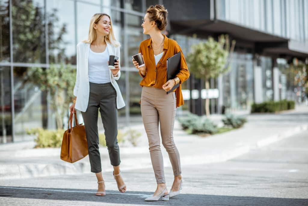zwei junge Geschäftsfrauen gehen mit Kaffeetassen in der Nähe ihres Bürogebäudes im Freien spazieren - Employer Branding