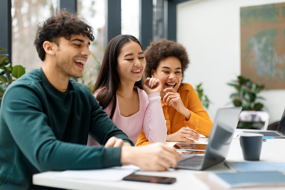 Trois amis heureux qui étudient ensemble dans un espace de coworking, des étudiants internationaux qui se préparent à un examen universitaire avec un ordinateur portable - PAE