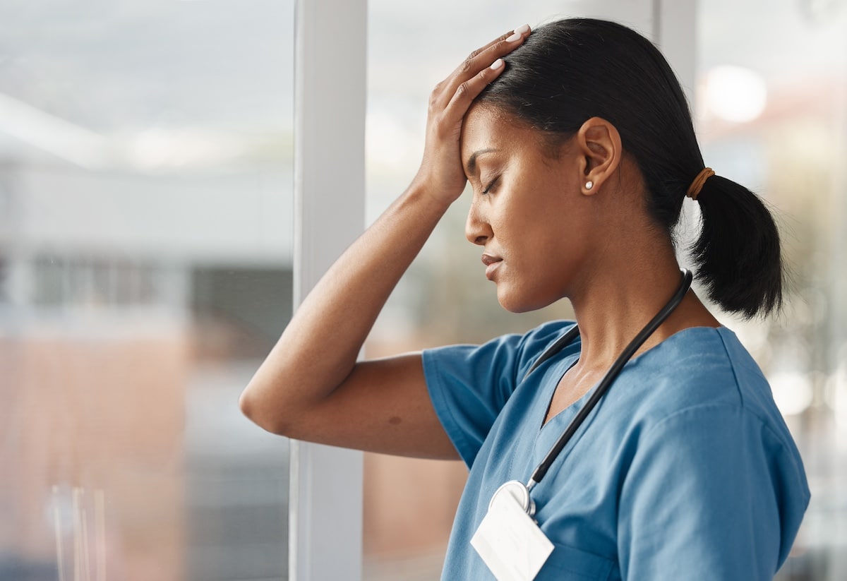 Mental health, doctor with headache and stress standing at window at hospital. Burnout or overworked, anxiety or depression and female nurse or caregiver holding her head for migraine pain at clinic.