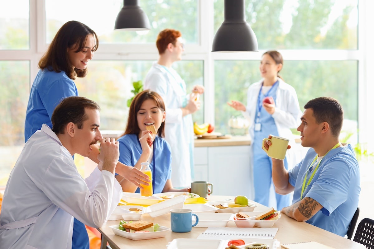 Team of doctors having lunch at table in hospital kitchen - Safeguarding caregivers' health