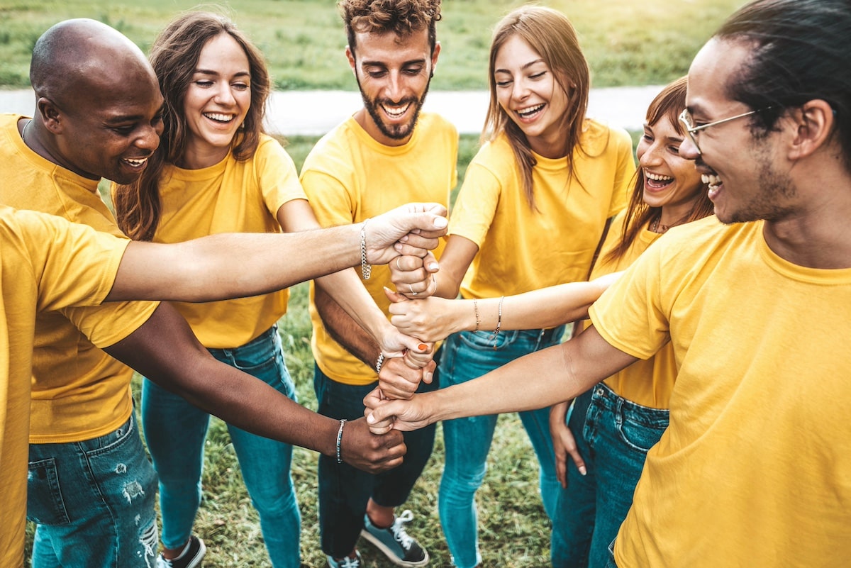 Multiracial happy young people stacking hands outside - Youth community concept with guys and girls standing together supporting each other -