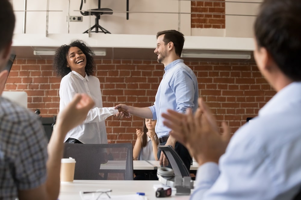 Happy ceo and team congratulating successful african american worker by shaking clapping hands, smiling black employee excited by reward bonus promotion, handshake as gratitude recognition concept -