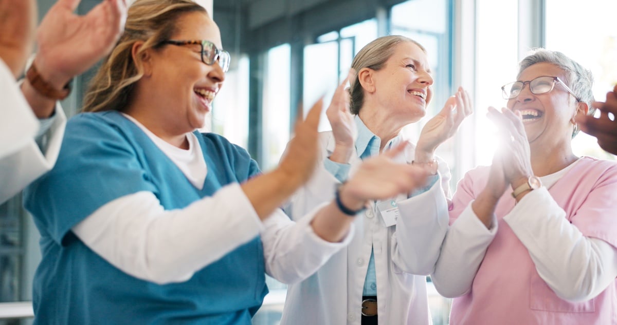 Doctor, support and applause in celebration for team unity, healthcare achievement or goal at the hospital. Group of medical professional clapping and celebrating teamwork, unity or victory at clinic. - protecting caregivers