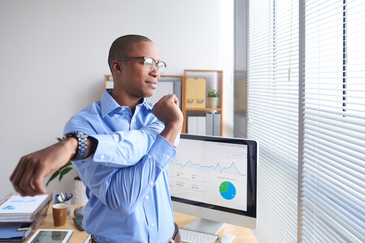 Smiling Black business executive stretching his arms during little break - wellbeing strategies