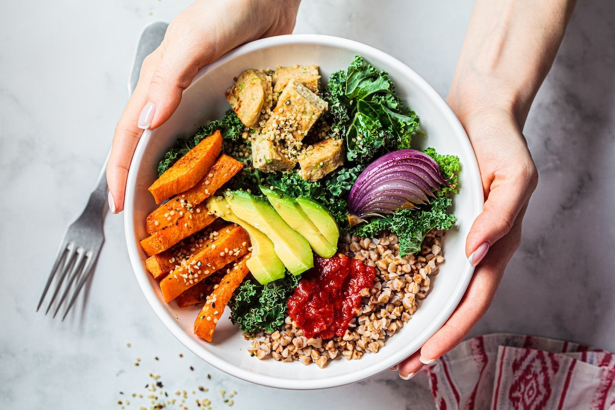 Baked vegetables, avocado, tofu and buckwheat buddha bowl. Vegan lunch salad with kale, baked sweet potato, tofu, buckwheat and avocado in a white bowl. Vegan concept. - health program