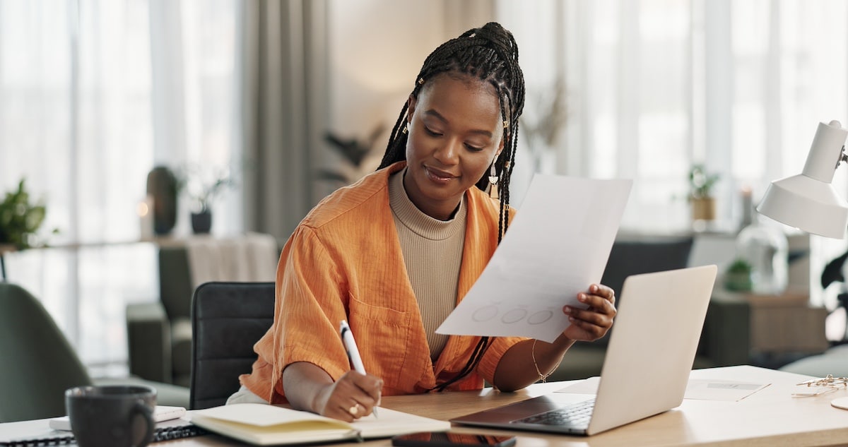 Black woman in home office, documents and laptop for research in remote work, ideas and thinking. Happy girl at desk with computer, writing notes and online search in house for freelance networking -