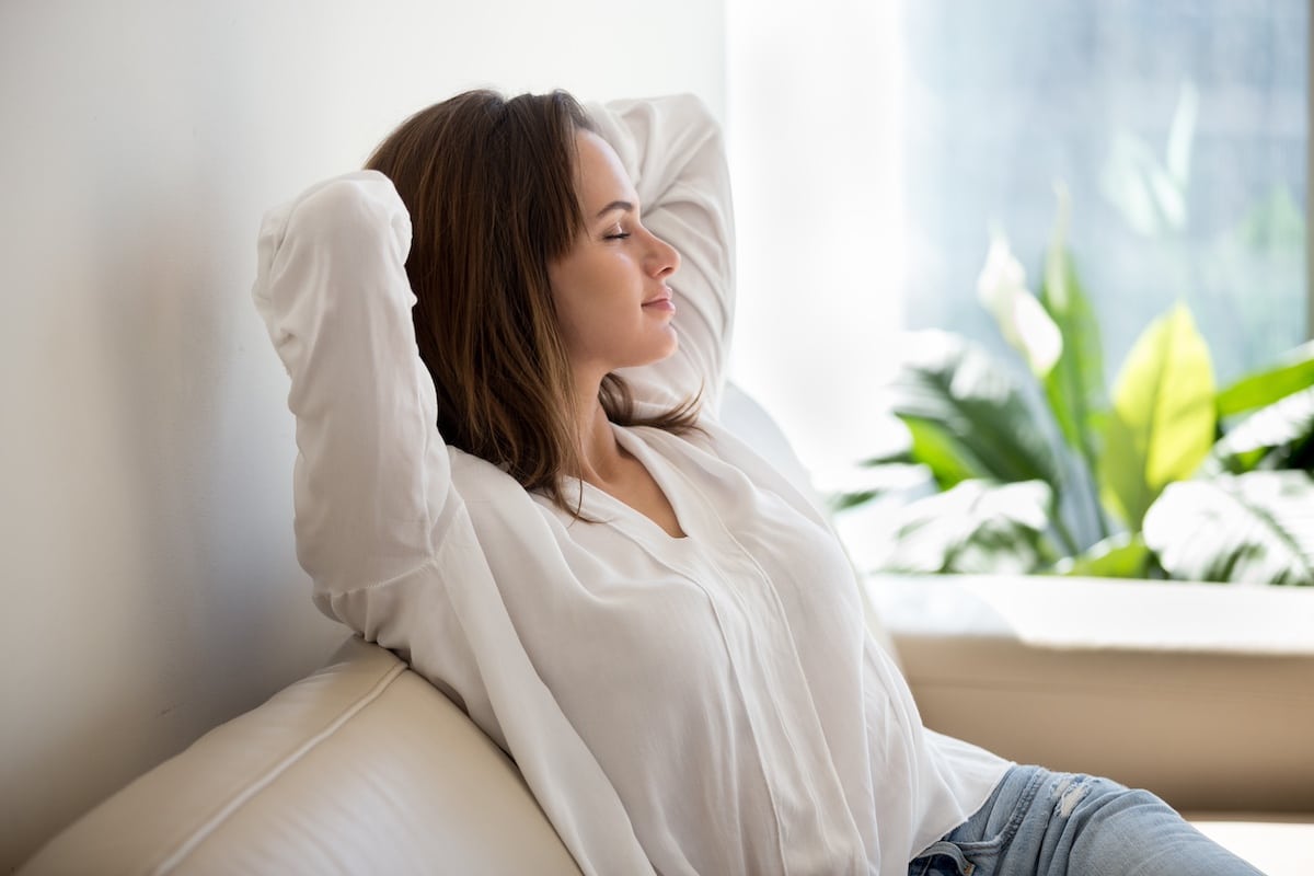 Entspannte Frau, die zu Hause auf dem Sofa frische Luft atmet -