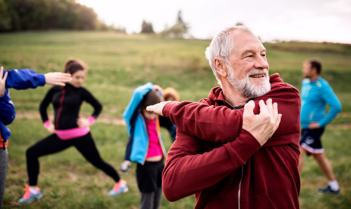 Eine große Gruppe fitter und aktiver Menschen, die in der Natur Sport treiben und sich dehnen. - Gesundheit am Arbeitsplatz