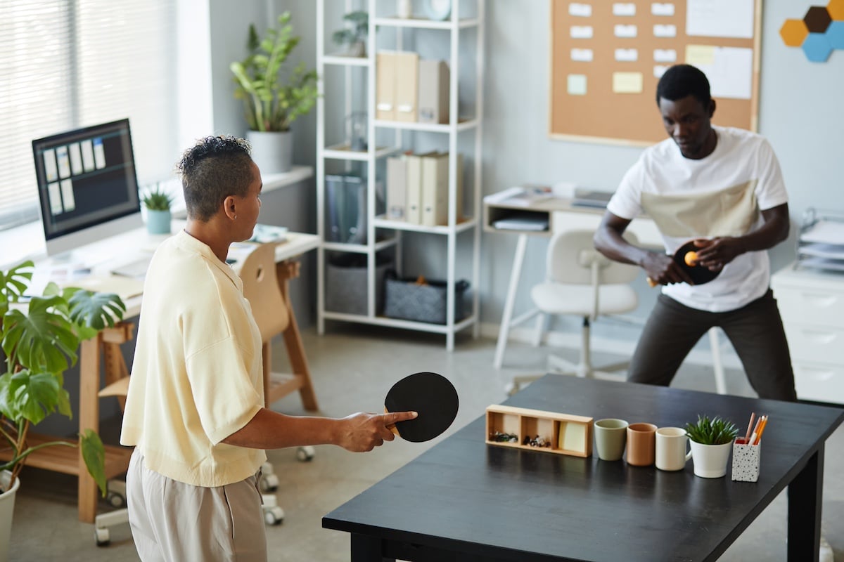 Hochwinkelporträt von zwei afroamerikanischen Jugendlichen, die im Büro Tischtennis spielen, Unterhaltungskonzept am Arbeitsplatz -