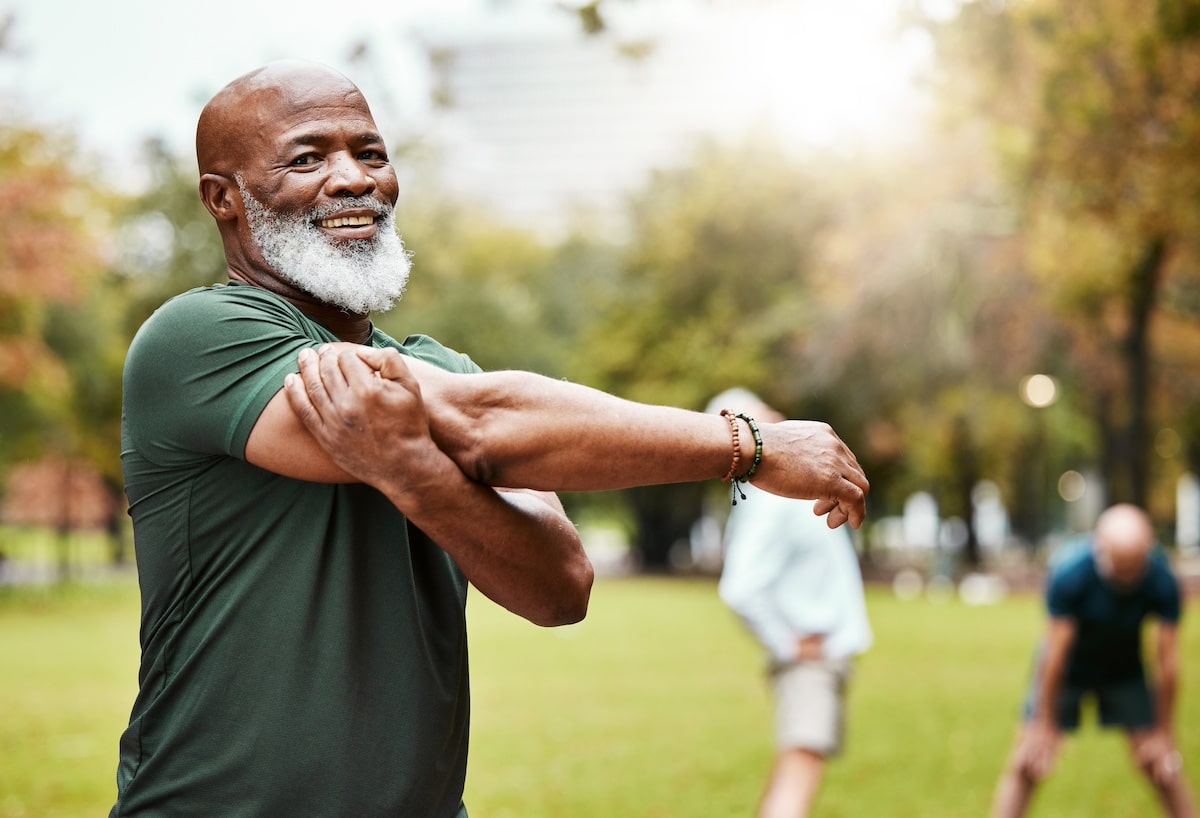 Porträt, Dehnübungen und aktive Senioren in einem Park für Training, Gymnastik und Cardio-Wellness. Fitness, Armdehnungen und Freunde mit älteren Männern entspannen sich vor dem Training, glücklich und gemeinsam für Aktivitäten. -