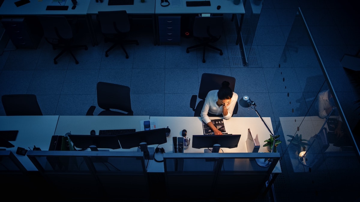 Spät abends im Büro: Geschäftsfrau benutzt Desktop-Computer, analysiert, verwendet Dokumente, löst Probleme, beendet Projekt. Aufnahme aus der Vogelperspektive -