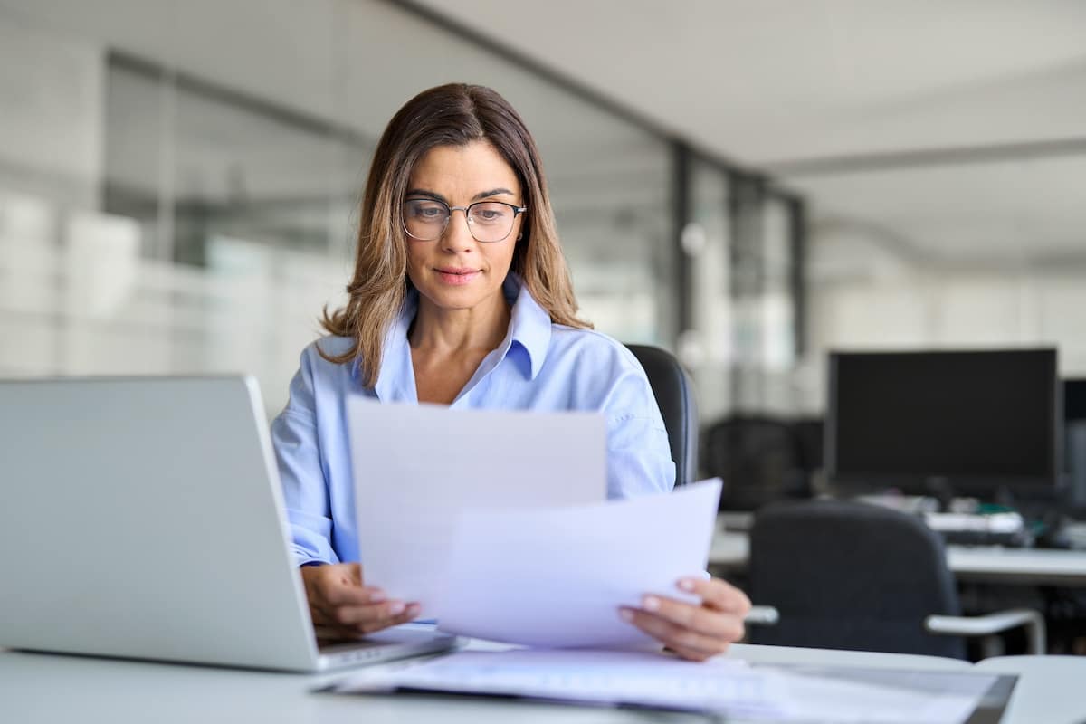 Busy mature business woman entrepreneur working in office checking legal document account invoice in office. Businesswoman of middle age manager executive or lawyer using laptop computer at work. -