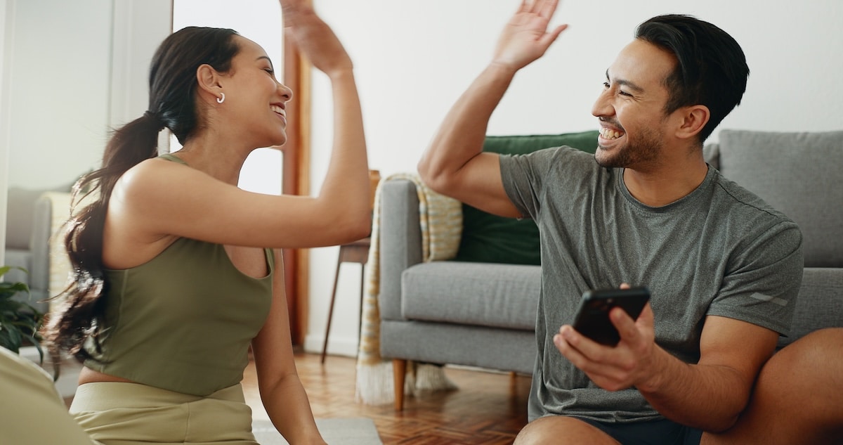 Happy couple, fitness and high five with phone for success, teamwork or workout goals together at home. Excited man or woman touching hands for winning, achievement or completion of exercise at house. - employee motivation